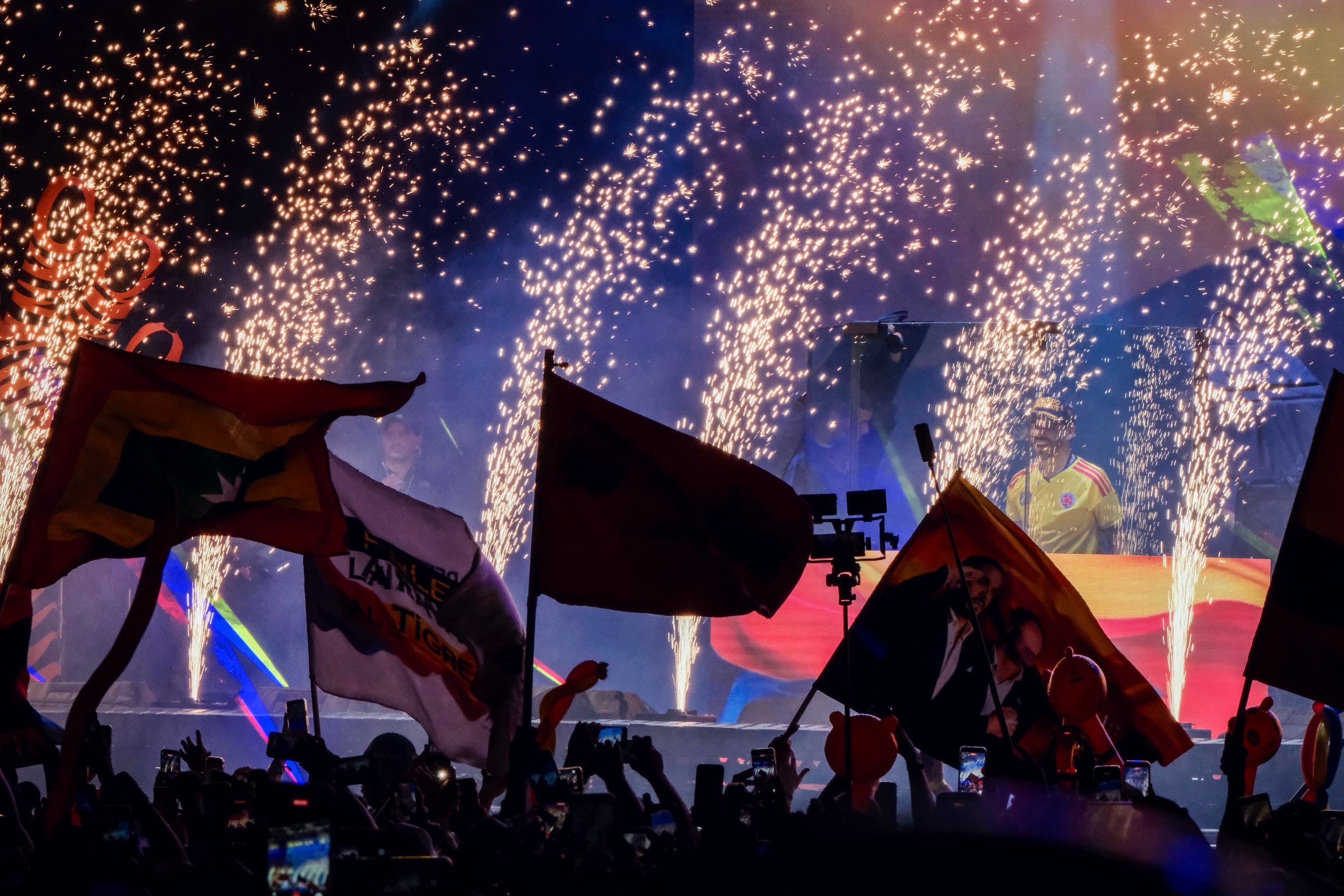 Fuegos artificiales y banderas sobre una multitud en un acto de campaña nocturno